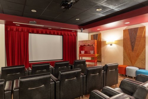 A cozy home theater with black chairs, a large screen, red curtains, and a snack stand in the corner.