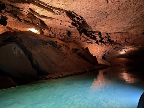 A serene underground cave with smooth rock formations and a calm, clear water pool reflecting soft light.
