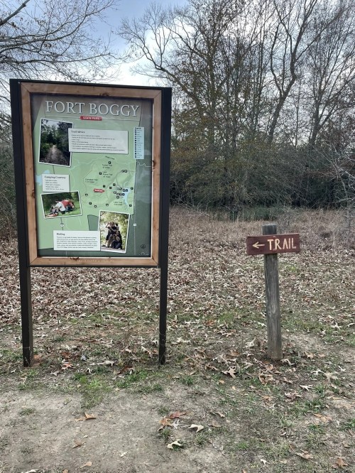 Sign for Fort Boggy with a map and trail direction, surrounded by trees and dry grass.
