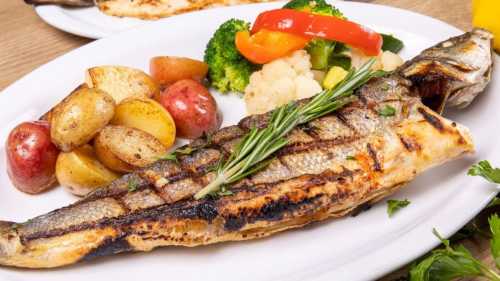 Grilled fish served with roasted potatoes and a colorful medley of steamed vegetables on a white plate.