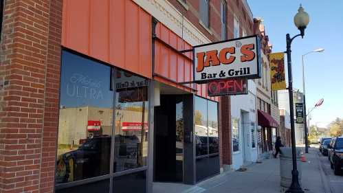 Exterior of JAC'S Bar & Grill with an "OPEN" sign, featuring brick walls and large windows.