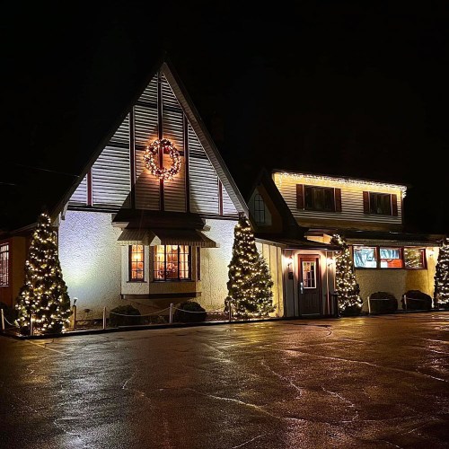 A charming building decorated with Christmas lights and trees, glowing warmly against a dark night sky.