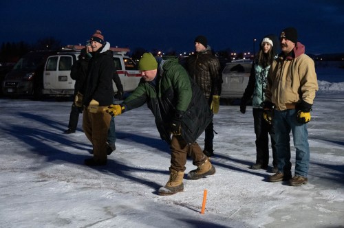 A group of people on an icy surface, one man throwing an object while others watch, dressed in winter clothing.
