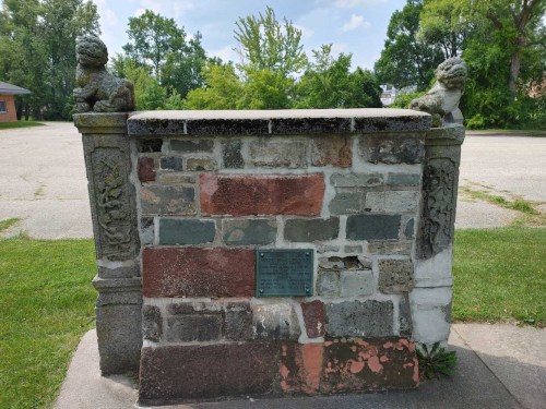 A stone monument with lion sculptures on each side, set in a grassy area under a clear blue sky.
