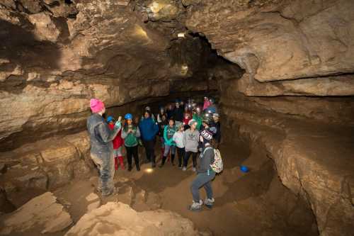 A group of people in helmets listens to a guide inside a cave, illuminated by headlamps and flashlights.