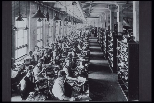 A historic black-and-white photo of a large office filled with workers typing on typewriters.