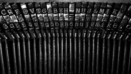 Close-up of vintage typewriter keys, showcasing metal typebars with letters and symbols in black and white.