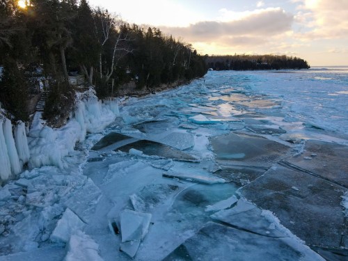 A frozen shoreline with ice formations and a calm lake under a cloudy sky.
