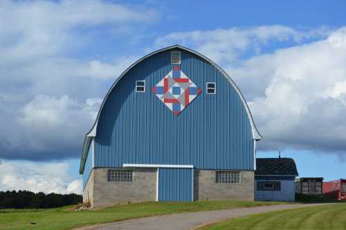 A blue barn with a quilt pattern on the front, set against a backdrop of blue sky and fluffy clouds.