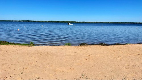 A serene beach scene with sandy shore, calm water, and a clear blue sky. A boat is visible in the distance.