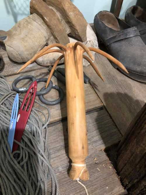 A wooden object with multiple protruding branches, resting on a wooden surface among tools and stones.