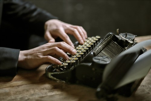A close-up of hands typing on a vintage typewriter on a wooden surface.