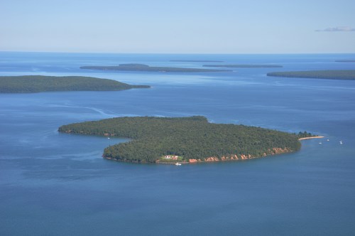 Aerial view of a lush green island surrounded by calm blue waters, with smaller islands in the distance.