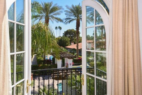 View from an open window showcasing palm trees, a pool, and a sunny courtyard.