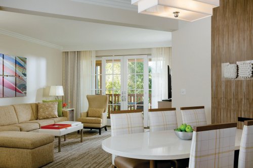 A modern living room with a sofa, armchair, dining table, and large windows overlooking a balcony.