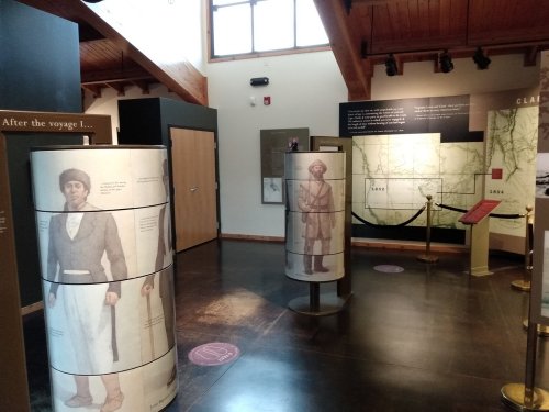 Exhibit interior featuring informational panels and cylindrical displays with historical figures and maps.