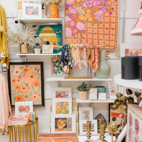 A colorful display of home decor, including artwork, vases, and accessories, arranged on shelves in a bright setting.