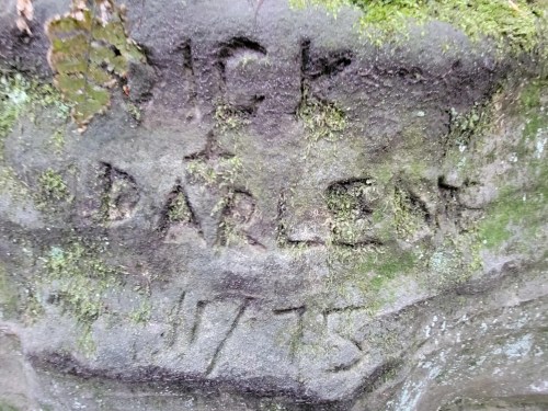 Carved inscription on a rock reading "J.G. Darlene 1775," surrounded by moss and natural textures.