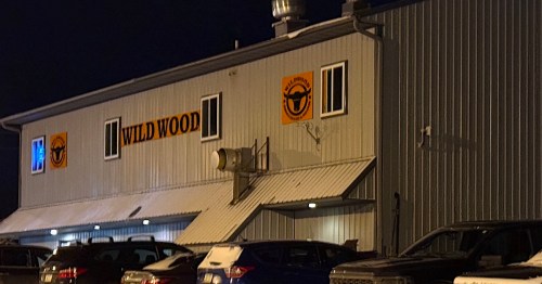 The exterior of Wildwood Smokehouse & Saloon in Iowa is illuminated at night, featuring the restaurant's steer skull logo on the metal siding above parked cars.