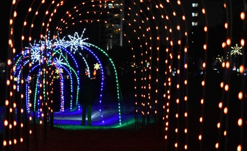 A person stands under a colorful light archway at night, surrounded by festive decorations and glowing patterns.