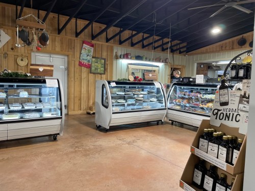 Interior of a rustic store featuring display cases with various baked goods and beverages, surrounded by wooden walls.