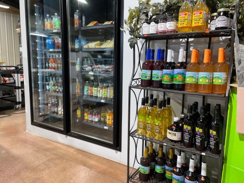 A display of beverages on shelves, with a glass-front cooler filled with drinks in the background.