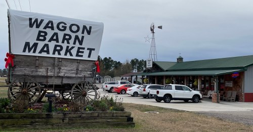A rustic market with a large sign reading "Wagon Barn Market," featuring a wagon display and a few parked cars.