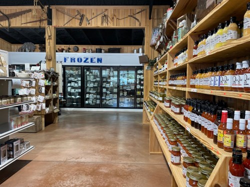 A grocery store aisle with shelves of jars and sauces, leading to a frozen food section in the background.