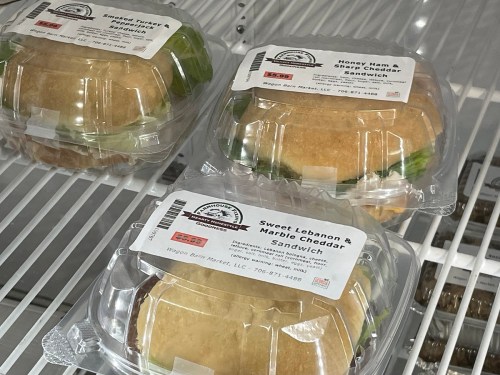 Three packaged sandwiches in a display case: Smoked Turkey, Honey Ham & Sharp Cheddar, and Sweet Lebanon & Marble Cheddar.