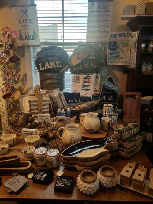 A display of lake-themed decor and gifts, including signs, pottery, and fishing items, arranged on a table.