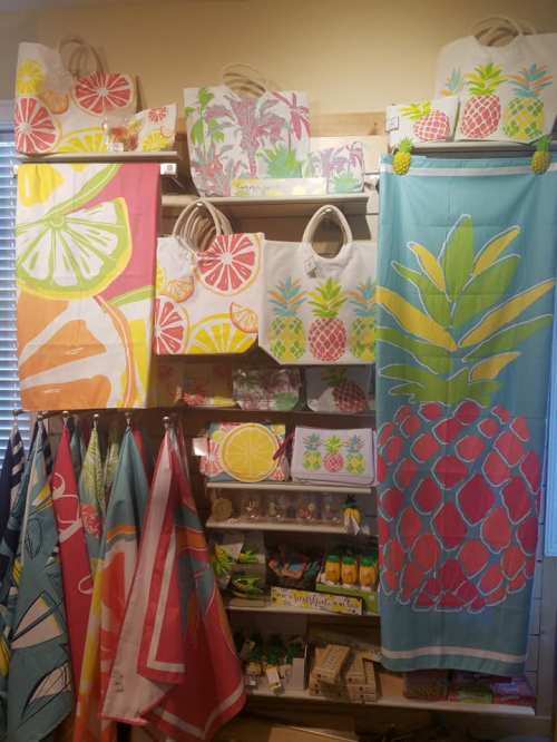 Colorful beach-themed bags and towels featuring pineapple and citrus designs displayed on shelves.