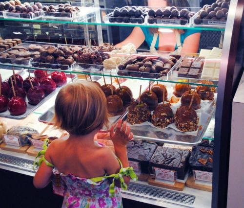 A child gazes at a display of various chocolates and candy treats in a shop.