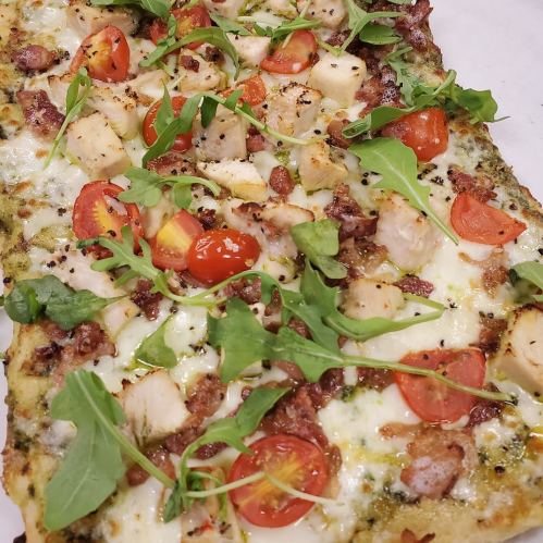 A rectangular pizza topped with chicken, bacon, cherry tomatoes, arugula, and a pesto sauce on a crispy crust.