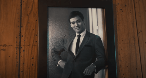 A black-and-white photo of a man in a suit, smiling confidently with one hand on his hip.