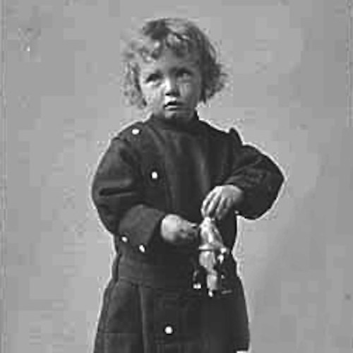A young child with curly hair holds a toy in a vintage black-and-white photograph.