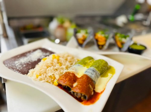 A plate of enchiladas with green and red sauce, served with rice, black beans, and a side of tacos.