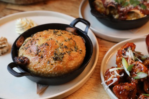 A golden, baked dish in a small cast-iron skillet, garnished with herbs, alongside other plates of food.