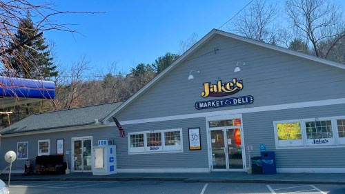 Exterior of Jake's Market & Deli, featuring a gray building with a sign, gas station, and clear blue sky.
