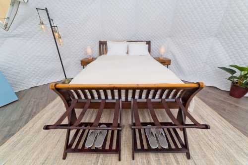 A cozy bedroom featuring a wooden bed, two side tables, and a rug, with slippers neatly placed on a bench.