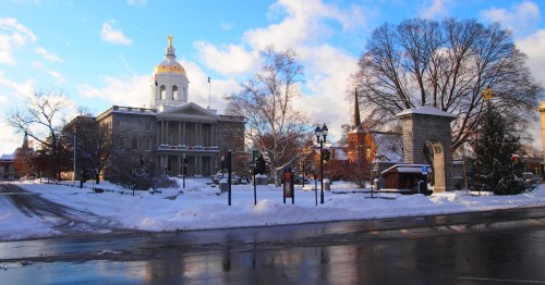 Snow-covered scene of a historic building with a golden dome, surrounded by trees and a clear blue sky.
