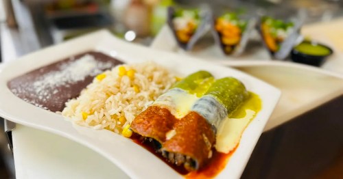 A plate of enchiladas with green and red sauces, served with rice, corn, and black beans.