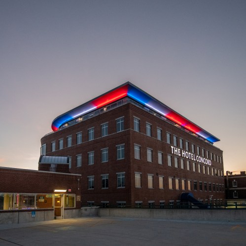 The Hotel Concord building illuminated at dusk, featuring colorful lights on the roof and a welcoming entrance.