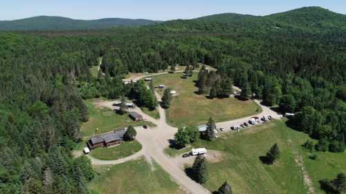 Aerial view of a wooded area with a campground, featuring several buildings and RVs surrounded by lush greenery.