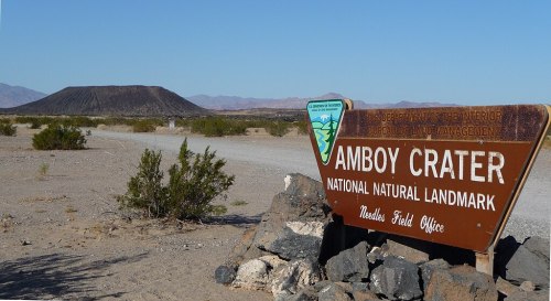 Sign for Amboy Crater National Natural Landmark with the crater in the background, surrounded by desert landscape.