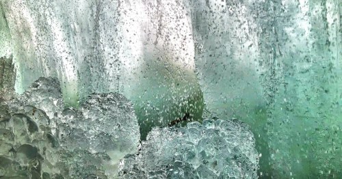 Close-up of cascading water with bubbles and splashes, creating a dynamic, textured surface in shades of green and white.