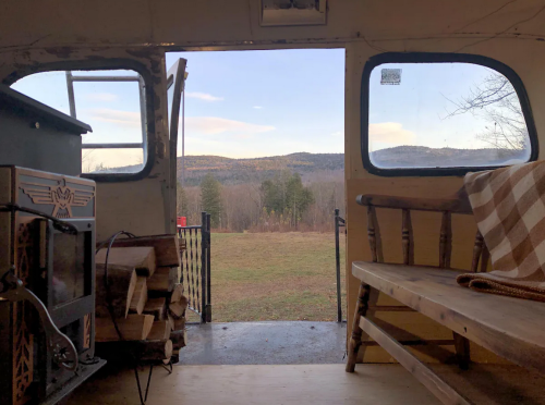 View from inside a cozy camper, showcasing a scenic landscape with mountains and a grassy field outside.