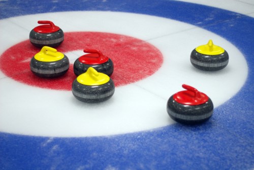 Six curling stones on a target, with three red and three yellow stones positioned on the ice.
