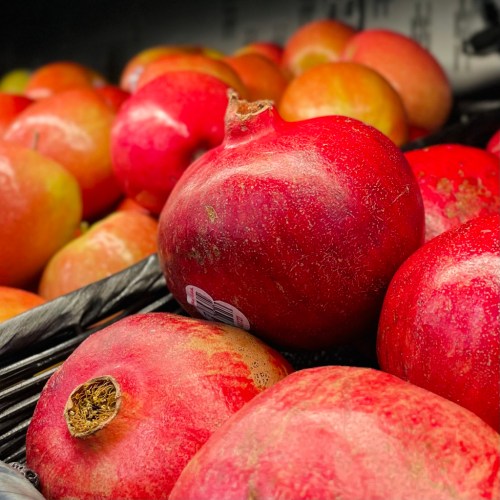 A close-up of red pomegranates among shiny red apples in a grocery display.