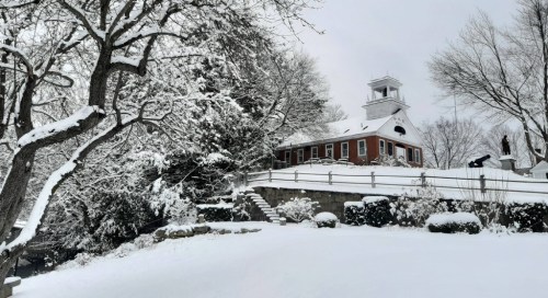 A snow-covered landscape featuring a red building, trees, and a staircase, all blanketed in fresh snow.