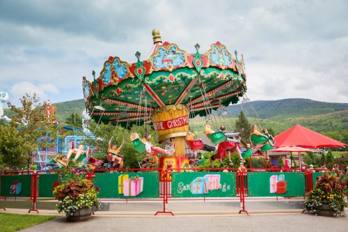 A colorful carousel ride at a festive amusement park, surrounded by greenery and mountains under a cloudy sky.